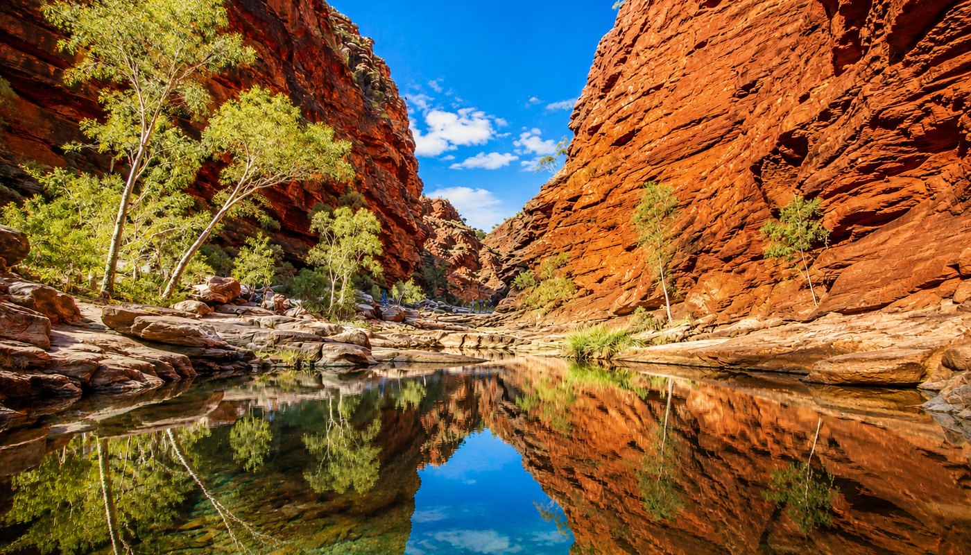 Sunlit red sandstone gorge with a still waterhole in Australia's Red Centre